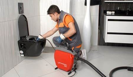 Yanındaki kırmızı tıkanık açma makinesi ile tuvaletteki tıkanıklığı açan usta görseli.
